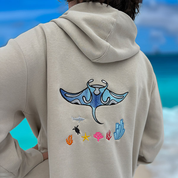 Back view of a sand-colored hoodie featuring an embroidered manta ray, shark, turtle, and coral reef